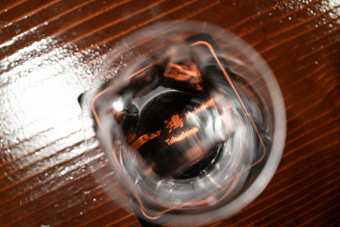 グラスの底に入った「Bar 鴻 Tokushima」の銅色ロゴを真上から捉えたカット