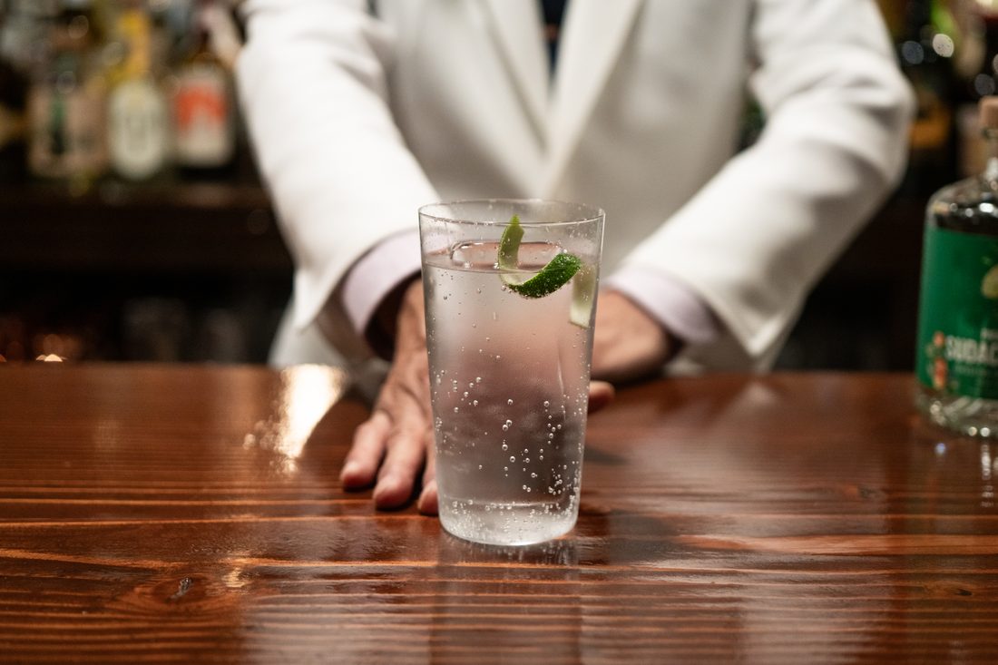 Premium Sudachi Ginのジントニック。ミントを添えたタンブラーをバーテンダーの手がカウンターに置く